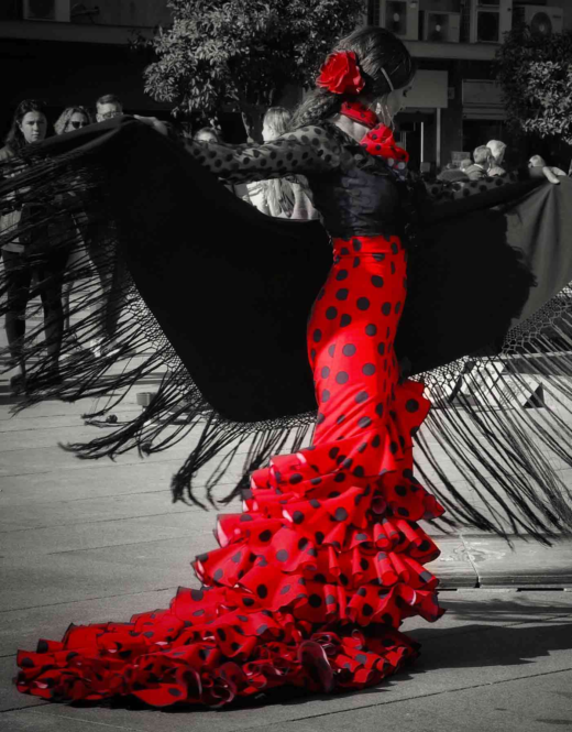 A woman dancing flamenco on the street. She wears a flamenco dress on a very intense red. The rest of the picture is black and white