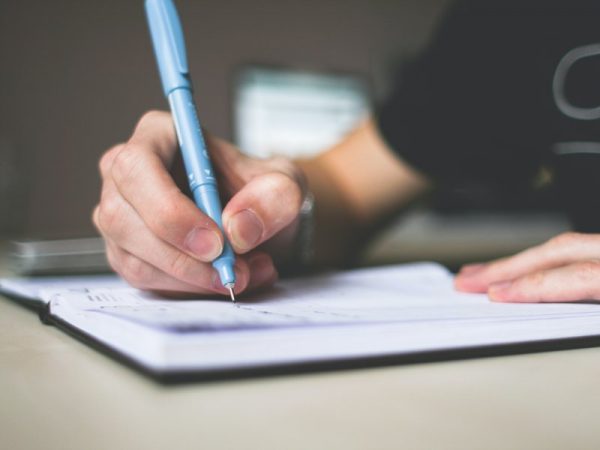 Woman's hand holding a blue pen while writing in a notebook