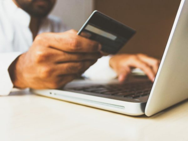 Man's hand holding a credit card while typing in his laptop